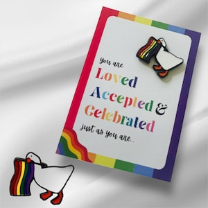 以下が含まれることがあります： 虹色の旗を持った白いガチョウ。カードには「You are Loved Accepted & Celebrated just as you are... 」と書かれています。