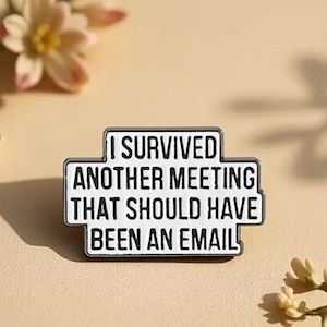Op de afbeelding: Witte emaille pin met zwarte tekst die luidt: "Ik heb een andere vergadering overleefd die een e-mail had moeten zijn."