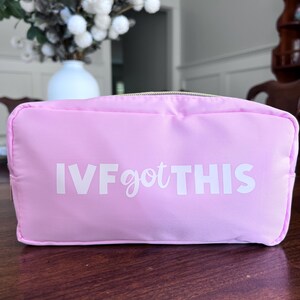 May include: A pink zippered pouch with the text "IVF got THIS" in white lettering.