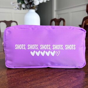 May include: A purple zippered pouch with the text "SHOTS, SHOTS, SHOTS, SHOTS, SHOTS" and a row of white hearts.