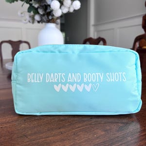 May include: A light blue zippered pouch with the text "Belly Darts and Booty Shots" and a row of white hearts.