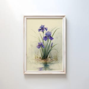 May include: Framed art print featuring a watercolor painting of purple iris flowers. The irises are surrounded by green leaves and are reflected in the water. The artwork is set in a white wooden frame.