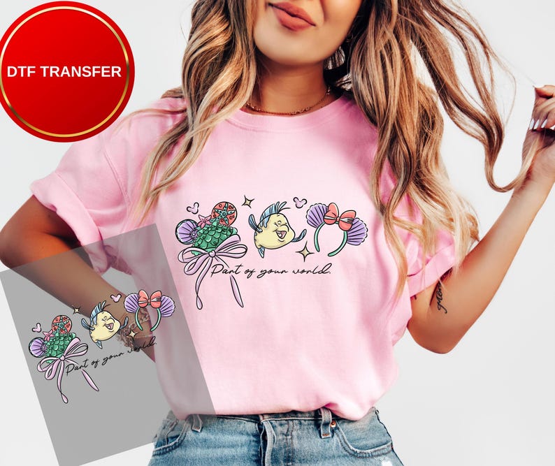 May include: Pink t-shirt featuring a colorful graphic of cartoon characters and the text "Part of your world." The design includes a fish, a seashell, and a bow. The shirt is a DTF transfer.