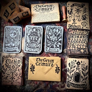 May include: A collection of printed paper ephemera including cards labelled Harvest Moon, Fairy Ring, Rosehip, and Mabon, a Green Grimoire booklet, a wax seal stamp, a September calendar, and an Elderberry Syrup card, all featuring black ink illustrations.