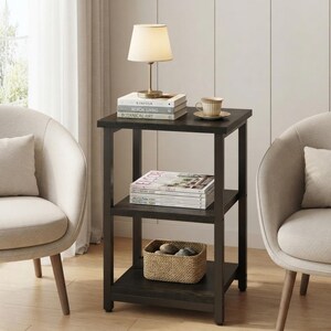 May include: A dark brown wooden side table with three square tiers. The top tier holds a small lamp, three stacked books, and a ceramic cup on a saucer. The middle tier holds a stack of magazines, and the bottom tier holds a woven basket.