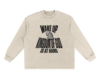 May include: A long-sleeved, cream-colored shirt with the text "WAKE UP KINGDOM OF GOD IS AT HAND" in black. The graphic includes praying hands. The shirt has a crew neck and a relaxed fit.