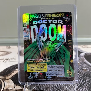 May include: A holographic Marvel Super-Heroes Doctor Doom trading card encased in a clear plastic protector. The card features comic book art of Doctor Doom with green and black colors, text detailing game abilities, and a 3/3 power rating.