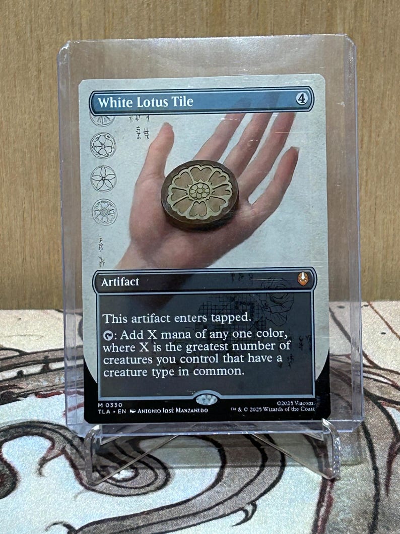 May include: A trading card titled "White Lotus Tile" with a brown, circular token featuring a white lotus design. The card is in a protective sleeve and includes text describing its artifact properties.