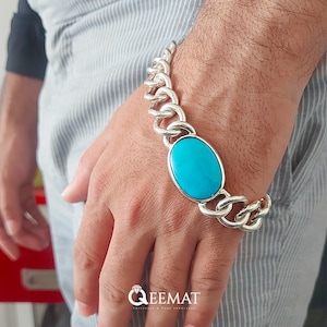 May include: Silver chain bracelet with a large, oval turquoise stone. The bracelet has a chunky link design. The turquoise stone is a vibrant blue colour. The bracelet is worn on a wrist.