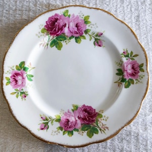 Op de afbeelding: Witte keramische plaat met een geschulpte rand en een gouden rand. De plaat is versierd met clusters van roze rozen en groene bladeren. Een klassiek en elegant ontwerp om eten te serveren.