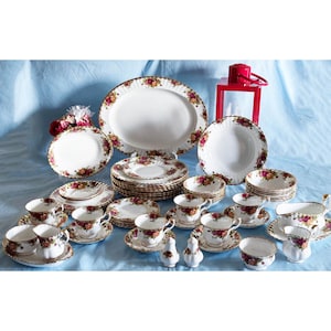 May include: A complete vintage china set featuring white porcelain pieces with a floral rose pattern and gold trim. The set includes plates, cups, saucers, bowls, and serving dishes. A red lantern is in the background.