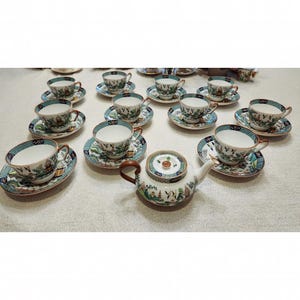 May include: A vintage tea set with a teapot and 10 cups and saucers. The set features a delicate floral pattern with blue, green, and gold accents. The cups and saucers are white with a gold rim.
