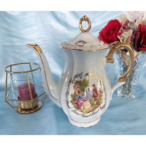 May include: White porcelain teapot with gold trim and a floral design featuring a couple in a garden scene. The teapot has a lid with a gold knob.