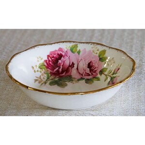 Op de afbeelding: Ovale witte porseleinen kom met een gouden rand. De kom heeft een bloemmotief van roze rozen en groene bladeren. Een decoratief stuk voor serveren of presenteren.