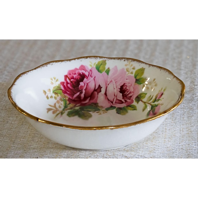 Op de afbeelding: Ovale witte porseleinen kom met een gouden rand. De kom heeft een bloemmotief van roze rozen en groene bladeren. Een decoratief stuk voor serveren of presenteren.