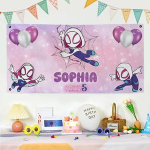 Puede incluir: Una pancarta rosa y morada con el nombre "Sophia" y la frase "is turning 5". La pancarta presenta ilustraciones de un personaje de superh&eacute;roe, junto con globos morados y plateados. La pancarta est&aacute; decorada con un dise&ntilde;o de telara&ntilde;a.