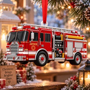 May include: A red fire truck Christmas ornament hanging from a red ribbon. The truck features a silver ladder on top, black tires with red hubs, and the name ARTHUR printed in white on the side above a gold fire department emblem.