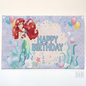 Puede incluir: Una pancarta de cumplea&ntilde;os con una ilustraci&oacute;n de sirena, pelo rojo y cola turquesa. La pancarta incluye globos, conchas marinas y algas. Las palabras "HAPPY BIRTHDAY" son turquesas. El fondo tiene un patr&oacute;n de escamas moradas claras.