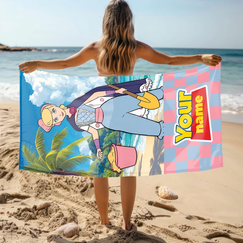 May include: A rectangular beach towel featuring a cartoon character with blonde hair wearing a blue outfit, holding a yellow shovel and a pink bucket on a beach background. The right side has a pink and blue checkerboard pattern with the text Your name.