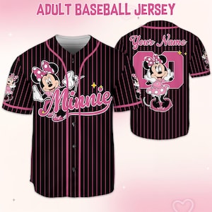 May include: Black baseball jersey with pink pinstripes, featuring Minnie Mouse graphics. The front displays "Minnie" in pink script, while the back has a pink number and space for a name. The jersey has a button-up front and short sleeves.