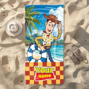 May include: A rectangular beach towel featuring a graphic of the character Woody from Toy Story wearing a lei and holding a blue and white striped life preserver on a tropical beach. The bottom section has a red and yellow checkerboard pattern with the text Your name.