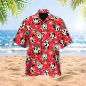 May include: Red short-sleeved button-down shirt featuring a festive pattern of Mickey Mouse, Donald Duck, Goofy, and snowflakes. The shirt has a black collar and is set against a beach background, evoking a holiday theme.