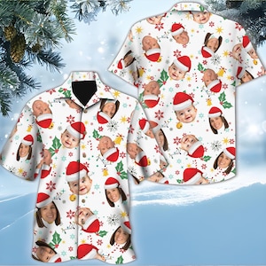 May include: White button-down shirt with a festive Christmas pattern. The design features faces wearing Santa hats, along with snowflakes, holly, and candy canes. The shirt is short-sleeved and has a black collar.