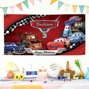 May include: A red banner featuring characters from the movie Cars, with the name "Jackson" and the number "5". The banner has a checkered flag design and the words "Happy Birthday". Party decorations are in the foreground.