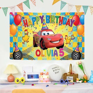 Peut inclure: Une banni&egrave;re d'anniversaire color&eacute;e avec une voiture de course rouge et le texte "HAPPY BIRTHDAY OLIVIA 5". La banni&egrave;re comprend des ballons, des confettis et des poulets de dessin anim&eacute;. Le fond est un motif &agrave; carreaux jaune et bleu.