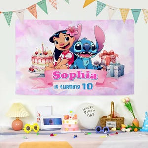 Op de afbeelding: Een verjaardagsbanner met Lilo en Stitch met de tekst "Sophia wordt 10". De banner heeft een roze aquarel achtergrond. Een taart, cadeaus en andere feestversieringen staan op de tafel hieronder.