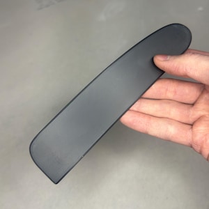 Puede incluir: Una pieza larga, delgada, negra, texturizada y rectangular de plástico.