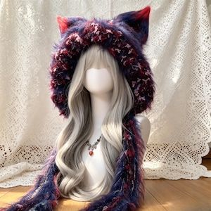 May include: A plush, fuzzy hooded scarf featuring pointed cat ears in a deep navy blue, purple, and vibrant red color palette. The hood is constructed from a textured, multi-tonal yarn with long, soft fibers and includes two long, matching scarf tails.