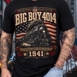 May include: A black t-shirt featuring a graphic of a steam locomotive with the text BIG BOY 4014, BUILDING AMERICA ONE MILE AT A TIME, THE WORLD'S LARGEST STEAM LOCOMOTIVE, and 1941, set against a distressed American flag background with Union Pacific branding.