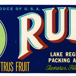 May include: A vintage citrus fruit label with a blue background and a white circle featuring a woman with dark hair. The label reads "PRODUCE OF U.S.A. RUBY LAKE REGION PACKING ASSN. CITRUS FRUIT Tavares, Florida BRAND".