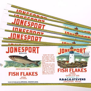 May include: A stack of eight vintage Jonesport brand fish flake labels. Each label features a lighthouse, a sailboat, and a fish. The label reads "Jonesport Brand Fish Flakes (Cod) Salt Added Contents 14 oz. Avoir. Packed by R.B.&C.G. Stevens, Jonesport, Maine."
