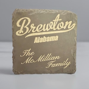 May include: A brown slate sign with gold lettering that reads "Brewton, Alabama, The Mcillian Family".