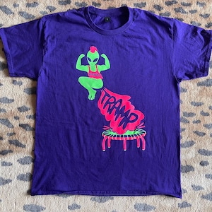 May include: Purple t-shirt with a green alien figure jumping on a trampoline with the word "TRAMP" in pink letters.