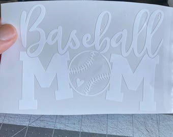 May include: White vinyl decal with the words "Baseball Mom" in a script font and block letters. A baseball with a heart detail is in the center. The decal is on a white backing.