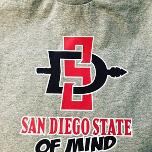 Peut inclure: T-shirt gris avec un logo rouge et noir qui dit "San Diego State of Mind".