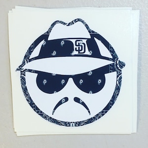 May include: A white sticker featuring a stylized face with a hat, sunglasses, and mustache. The hat and sunglasses are navy blue with a paisley pattern. The hat has the letters "SD" in white.