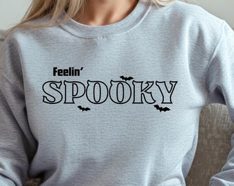 May include: A light gray sweatshirt with the words "Feelin' Spooky" in black, with bat graphics. The sweatshirt is a crew neck style.
