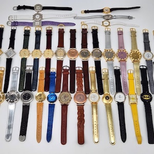 May include: A collection of various wristwatches with different band colors and styles. The watches feature gold, silver, and black watch faces with leather, metal, and fabric bands. Some watches have decorative elements.