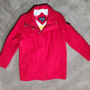 May include: A bright red jacket featuring a high collar, long sleeves, and a front button closure. The interior lining displays a geometric pattern in white, red, and yellow. A Pendleton brand label is visible on the inside neck area.