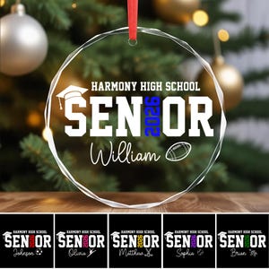 May include: A clear, round glass ornament with the text "HARMONY HIGH SCHOOL SENIOR 2026 William" in white. A graduation cap and football graphic are included. A red ribbon is attached for hanging. Additional ornaments with different names and sports are shown below.