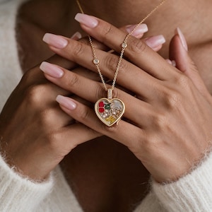 May include: A gold heart-shaped locket pendant necklace featuring a clear center filled with small decorative elements including red cherries, white pearls, and yellow floral accents. The gold chain includes small inset clear stones.