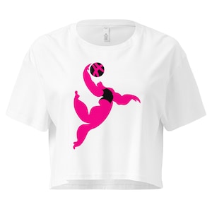 May include: White crop top featuring a stylized illustration of a person playing volleyball. The figure is rendered in bright pink with a black accent, holding a black and pink ball. The shirt has a crew neck and short sleeves.