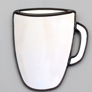 May include: A white ceramic mug shaped mirror with a black metal frame. The mirror is shaped like a coffee mug with a handle.