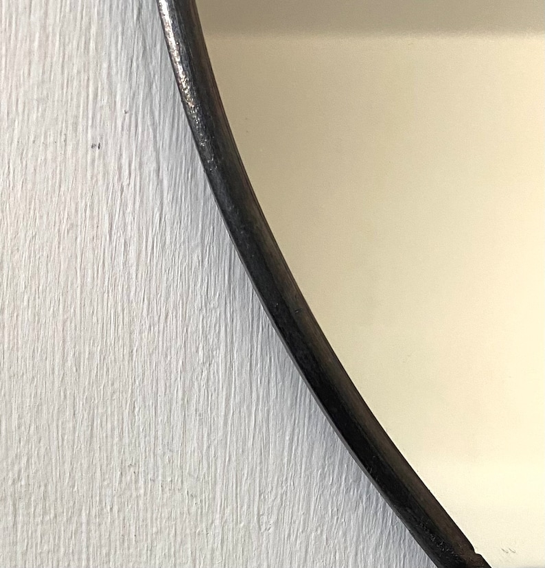 May include: Close-up of a white painted wooden surface with a black curved edge. The edge is smooth and appears to be part of a mirror frame.