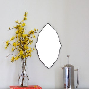 May include: A silver French press coffee maker sits on a white countertop next to a vase of yellow flowers and a book titled "Design Sponge at Home".