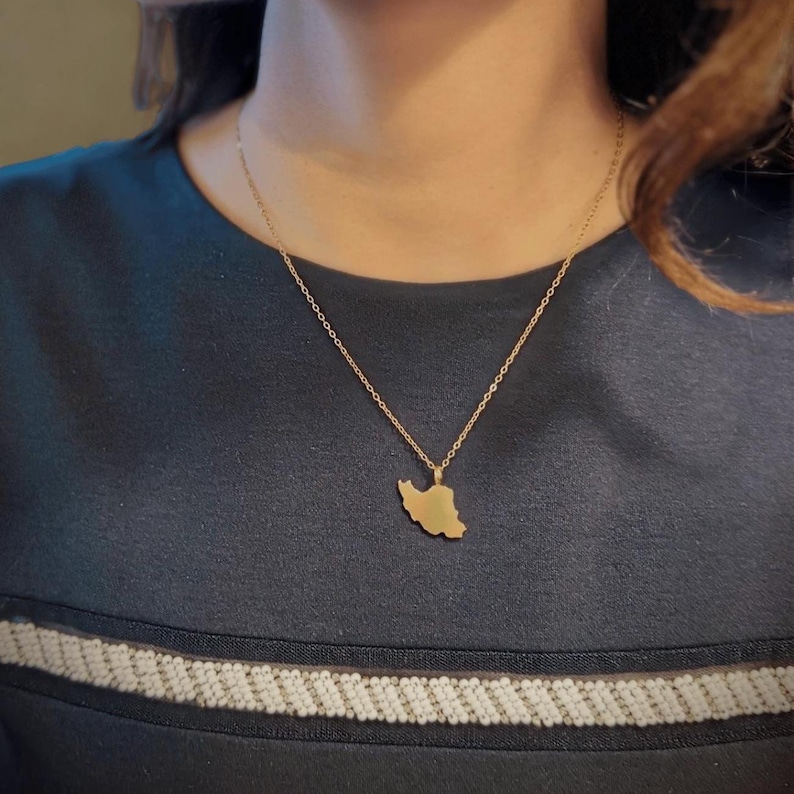 Peut inclure: Un collier dor&eacute; avec un pendentif en forme de la carte de l'Iran. Le pendentif est suspendu &agrave; une fine cha&icirc;ne. Le collier est port&eacute; sur un haut bleu fonc&eacute;.